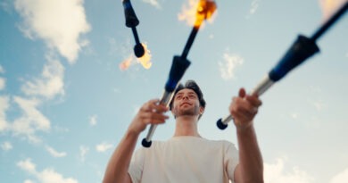 Ein Jongleur wirft brennende Fackeln vor blauem Himmel.