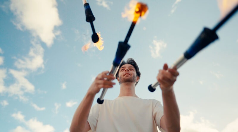 Ein Jongleur wirft brennende Fackeln vor blauem Himmel.