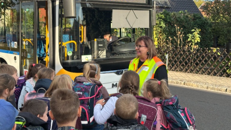 Kinder mit Schulranzen stehen bei einer Busschule vor einem Linienbus